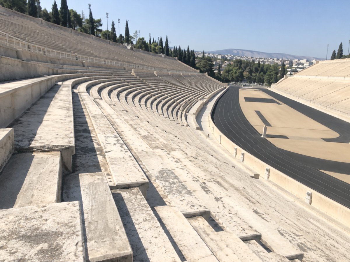 Leere weiße Marmortribünen des hufeisenförmigen Stadions in Athen bei grellem Sonnenlicht, schräg fotografiert.