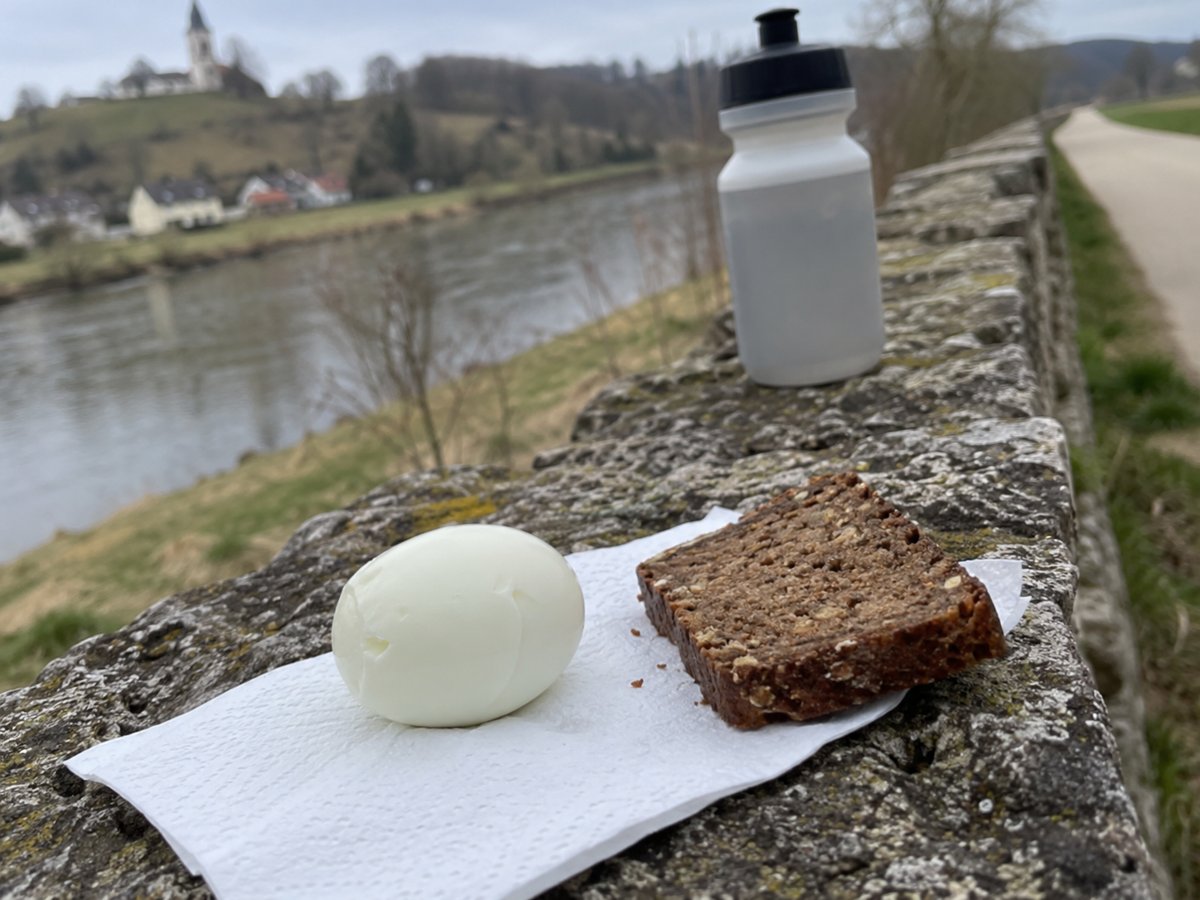 Ein geschältes gekochtes Ei und eine Scheibe dunkles Roggenbrot auf einer Serviette auf einer Steinmauer am Fluss.